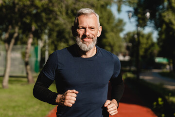 Cropped closeup portrait of a male mature athlete sportsman runner jogging in the morning in public park. Slimming exercises, active seniors concept.