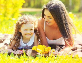 Wall Mural - Portrait of happy laughing mother with little girl child lying on the grass on sunny summer blurred background