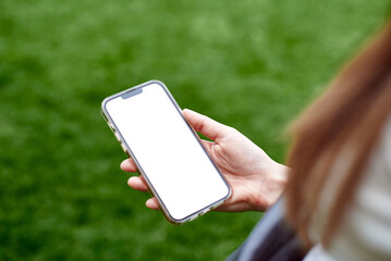 The girl holds the phone with a blank screen, view from the back. Advertise your app. Mockup image of hand holding white mobile phone with blank white.