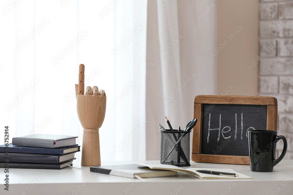 Wooden hand with stationery, chalkboard and cup on table in office