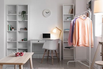 Poster - Interior of light room with modern workplace, rack and hoodies