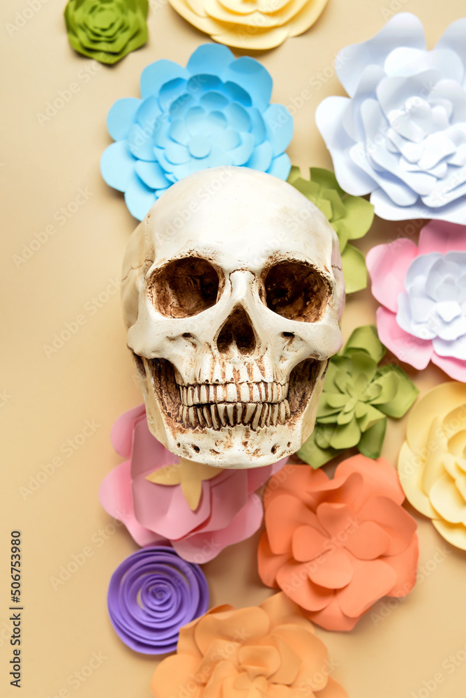 Human skull with handmade paper flowers on beige background