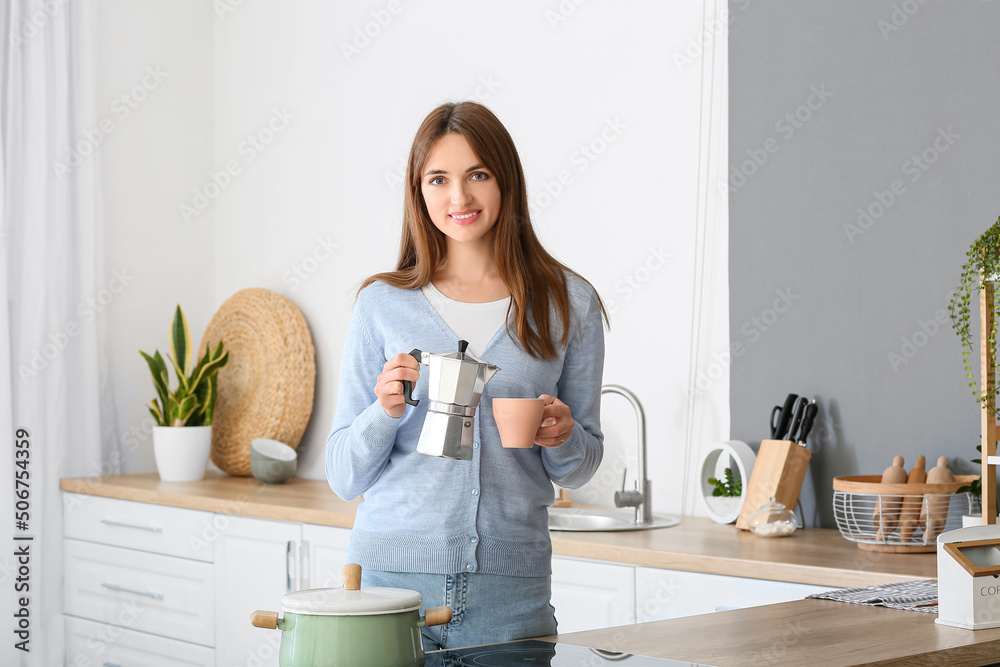 Pretty young woman with coffee maker and cup in kitchen