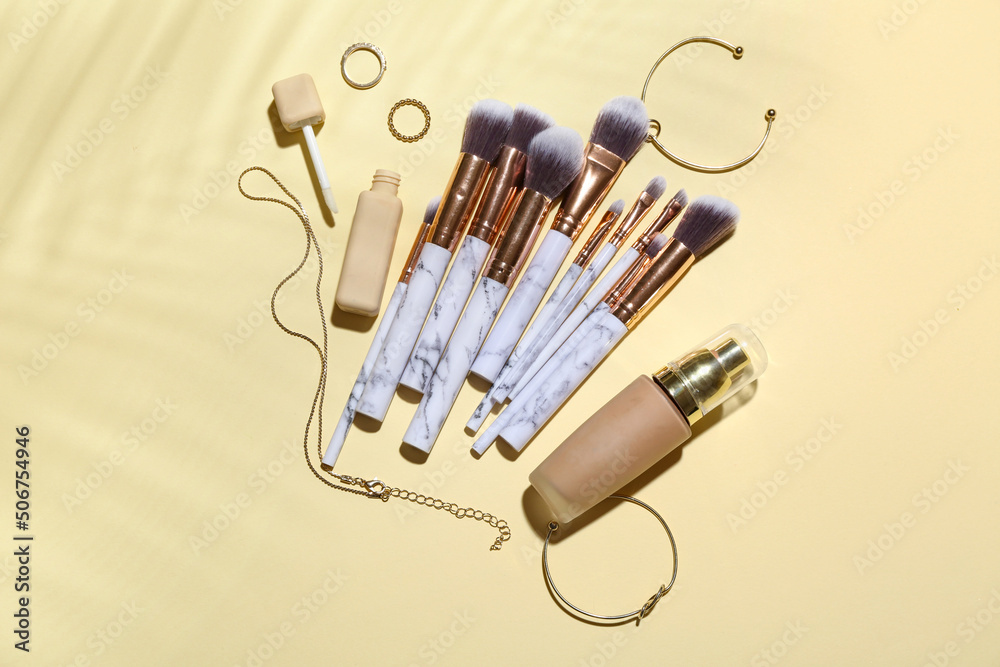Makeup brushes with jewelry and cosmetics on color background