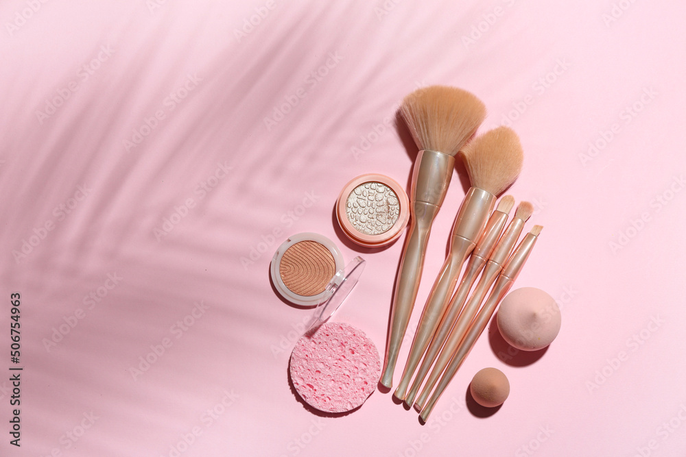 Makeup brushes with sponges and cosmetics on pink background