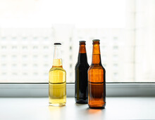Bottles With Craft Beer On The Windowsill, Against The Backdrop Of A Multi-storey Building. Dark And Light Varieties Of Homemade Home-brewed Beer