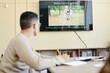 © pressmaster - Selective focus on background shot of unrecognizable young man sitting at table watching video or presentation during English lesson