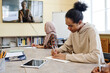 © pressmaster - Multi-ethnic students sitting at table watching educational video and making notes in notebooks during lesson