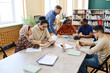 © pressmaster - Mature Caucasian English language teacher helping immigrant students with doing task during lesson in library