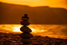 Pebble Pyramid Silhouette On The Beach. Sunset With Sea In The Background. Zen Stones On The Sea Beach Concept, Tranquility, Balance. Selective Focus