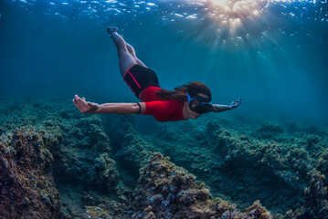 Girl diving holding the breath with rays of sun entering the water in the background