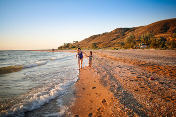 Wall Mural - Sister girls in swimsuits run and play on the seashore, free summer vacation and happy children