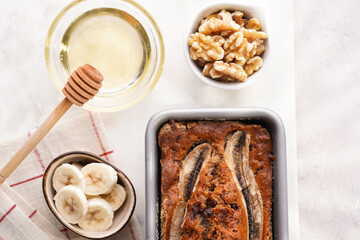 Wall Mural - Chocolate banana bread with walnuts in a metallic baking mold and ingredients on a grey neutral background with creative lighting, top view