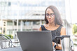 © weyo - Female student sits outdoors in teh city with a reusable takeaway coffee mug studying from a laptop