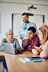 Multiracial group of students e-learning on laptop in classroom at university.