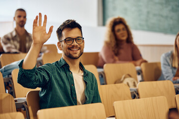 Wall Mural - Happy college student raising his hand to ask question during class.