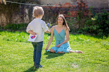 Poster - Beautiful kid and mom in spring park, flower and present. Mother getting gift from toddler boy for Mothers day