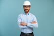 Young architect man with happy face in builder safety helmet smiling while looking at the camera and posing arms crossed over isolated background