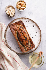 Wall Mural - Chocolate banana bread with walnuts on a white plate with brown rim and ingredients on a grey neutral background , top view