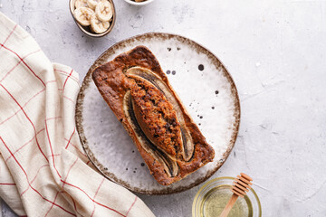 Wall Mural - Chocolate banana bread with walnuts on a white plate with brown rim and ingredients on a grey neutral background , top view