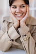 © LIGHTFIELD STUDIOS - portrait of happy woman in beige trench coat smiling outside.