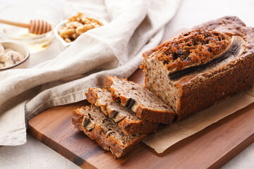 Wall Mural - Chocolate banana bread with walnuts on a wooden board and ingredients on a grey neutral background