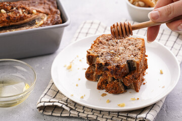 Wall Mural - pouring honey onto Slices of Chocolate banana bread with walnuts on a checkered kitchen napkin and ingredients on a grey neutral background