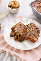 Wall Mural - Slices of Chocolate banana bread with walnuts on a pink kitchen napkin and ingredients on a grey neutral background with creative lighting