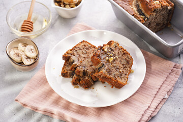 Wall Mural - Slices of Chocolate banana bread with walnuts on a pink kitchen napkin and ingredients on a grey neutral background with creative lighting