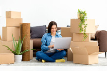 Moving To A New House, Rental Housing. Happy Caucasian Woman Using Laptop Computer To Search And Order Transportation Service And Movers To Move To A New Home