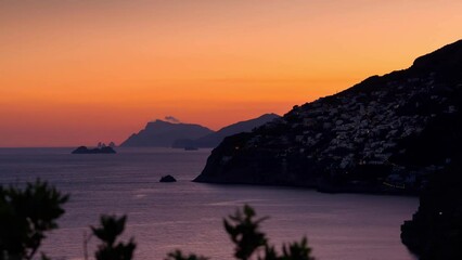 Wall Mural - Timelapse video of sunset on the Amalfi Coast with the small town of Praiano on the left and the island of Capri far away on the horizon.