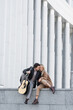 full length view of joyful couple in stylish autumn outfit sitting with acoustic guitar on parapet.