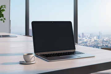 Blank black laptop screen with copyspace for your logo or text on light wooden table with coffee mug in sunny room with city view from big window. 3D rendering, mockup