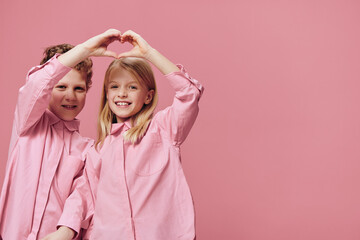 cute, beautiful children boys and girl show their hearts with their hands, standing in pink clothes on a pink background