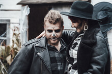 Scary Love Family Couple Man, Woman Celebrating Halloween.Terrifying Black Skull Half-face Makeup,witch Costumes,stylish Images,jacket,hat.Horror,fun At Photoshoot, Holiday Party Near Barn On Street