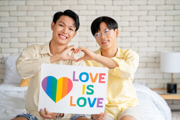 Couple gay or lgbt man sit on bed and hold banner to express their feeling and proud their relationship.