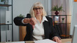 Upset senior mature business woman showing thumbs down sign gesture, expressing discontent, disapproval, dissatisfied, dislike at home office, using laptop computer. Elderly grandmother freelancer