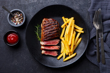 Wall Mural - Beef Steak medium rare with French fries on a black plate. Dark background. Close up. Top view.