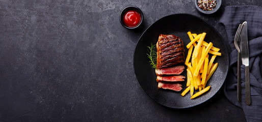 Wall Mural - Beef Steak medium rare with French fries on a black plate. Dark background. Copy space. Top view.