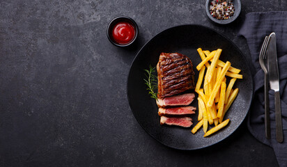 Wall Mural - Beef Steak medium rare with French fries on a black plate. Dark background. Copy space. Top view.