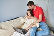 © Elena - young couple on the sofa. a woman works on a laptop, a man hugs from the back and kisses the top of his head
