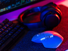 Close-up. The computer keyboard, mouse and headphones are on the desktop. Accessories, a large group of objects. Office, business, music, video games. Neon lighting.