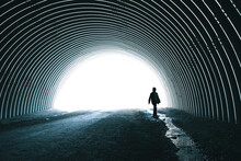 Child Walking Alone Beside Stream Running Through Dark Metal Tunnel.