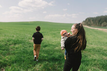 A Woman Walks With Her Children On A Green Meadow