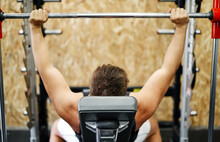 Unrecognizable Young Man Exercising In Gym With Bench Press