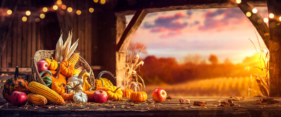 Wall Mural - basket of pumpkins, apples and corn on harvest table in barn with open door and sunset background - 