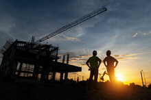 Engineers And Workers Inspecting Projects At The Construction Site Background. Construction Site At Sunset In The Evening, Asian Engineer Silhouette