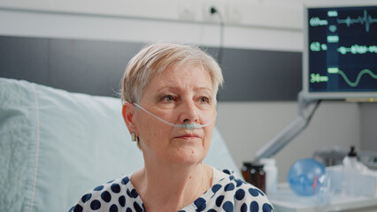 close up of aged woman sitting in bed with heart rate monitor at clinic. portrait of patient with il