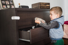 A Small Child Opens A Chest Of Drawers With Clothes And Goes Through The Lingerie In The Closet. Children's Curiosity And Parental Control. Drawer Latch. Child Safety At Home