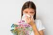 Woman with closed eyes sneezing in tissue holding colorful bouquet of wild flowers